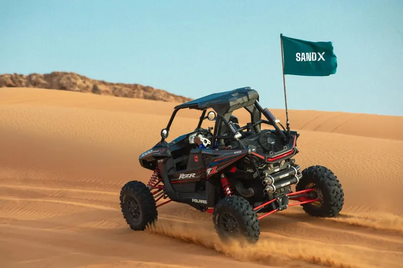 Polaris RZR RS1 single-seat dune buggy throwing sand under a SAND X flag